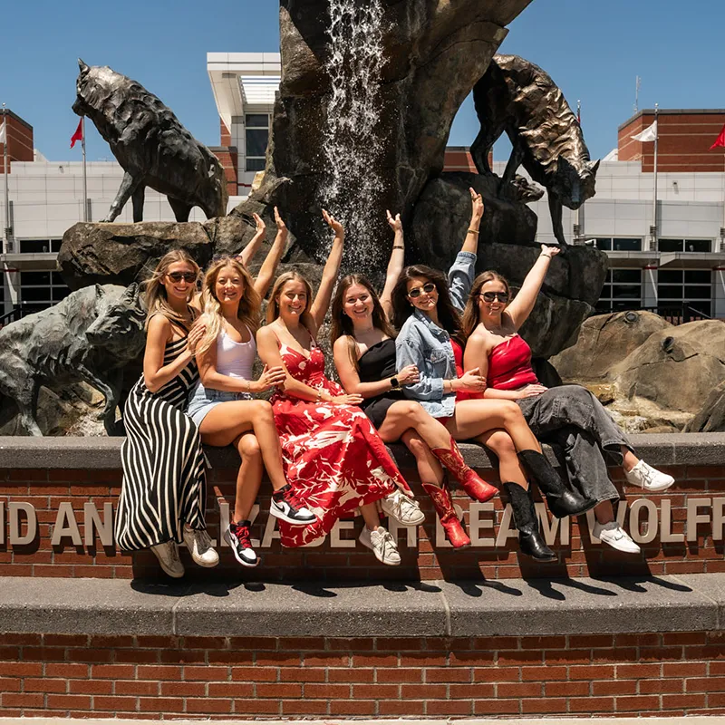 Group of girl friends posed sitting in front of the Wolfpack fountain