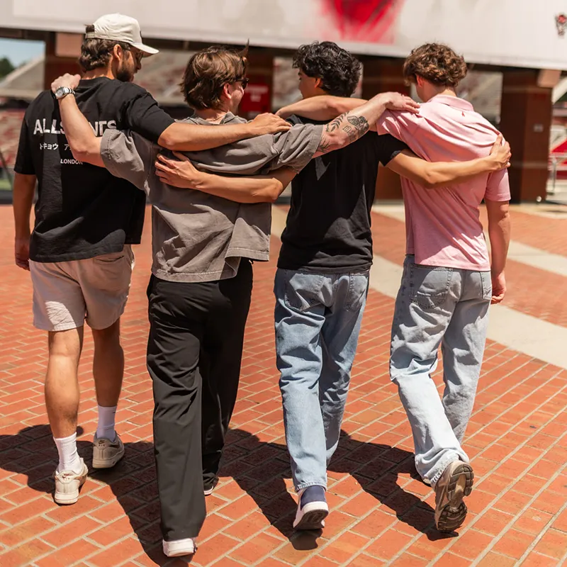 Four guys with arms over shoulders walking into Carter-Finley Stadium