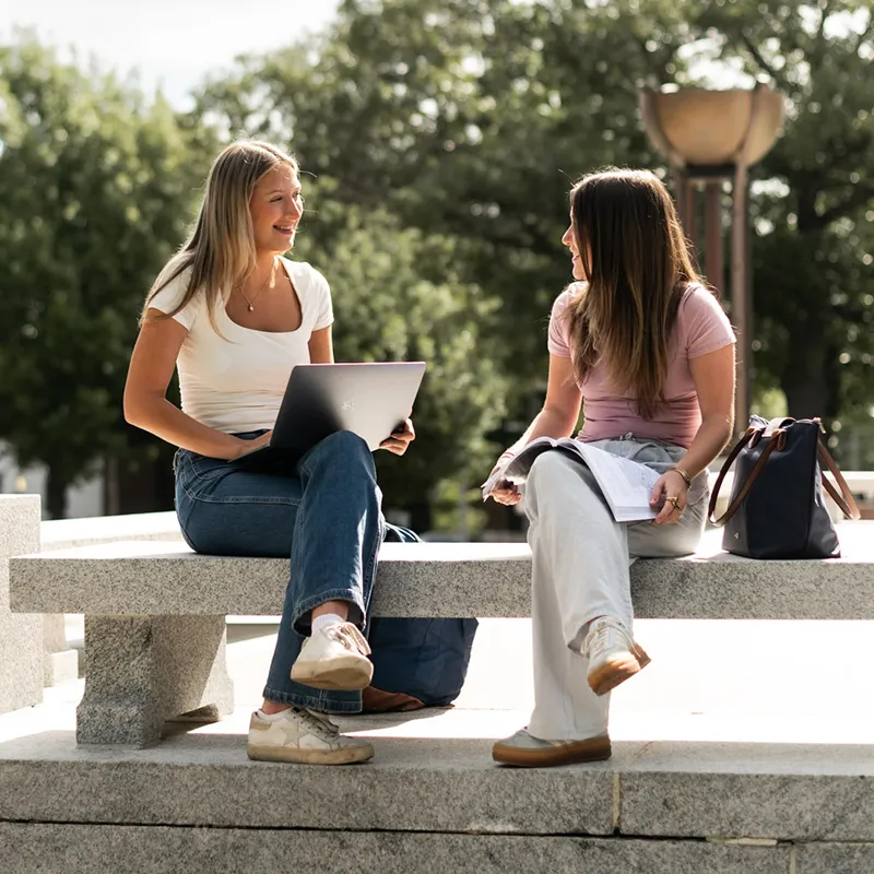Friends sitting on bench outside studying