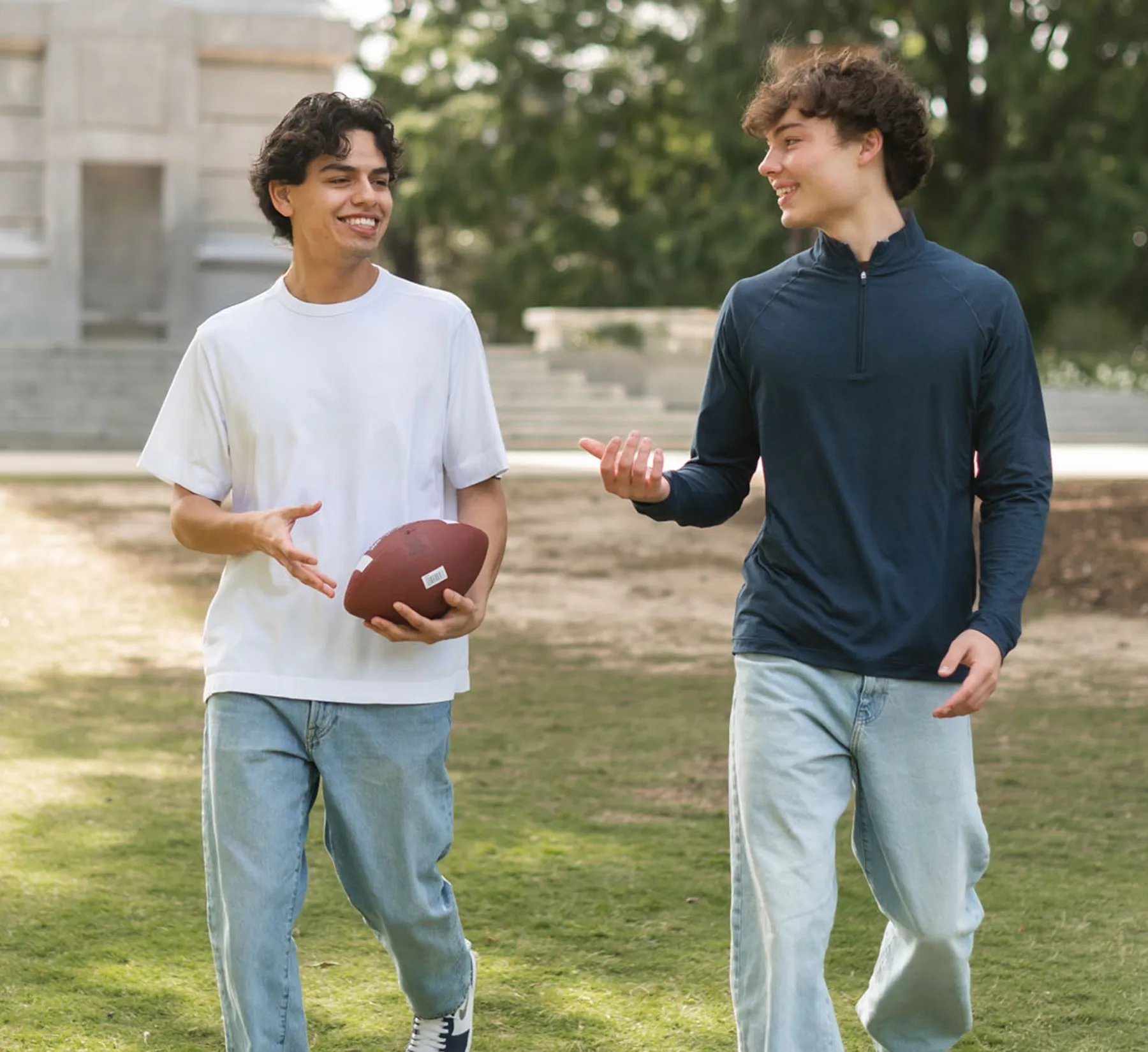 Guys chatting walking holding football in front of 